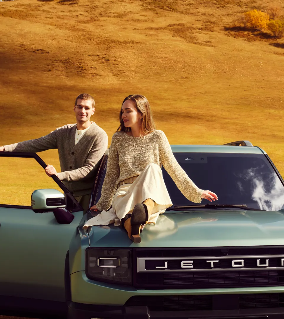 Couple sitting on Jetour hood in golden field